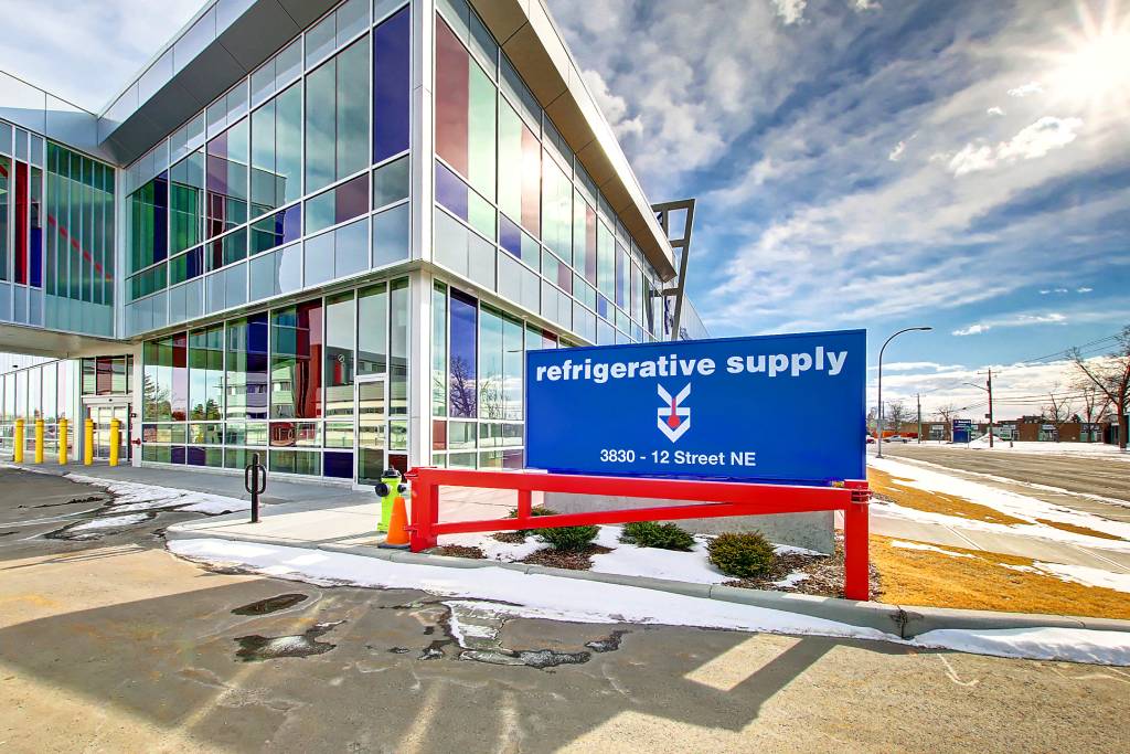 A close-up of the Refrigerative Supply. The sun shines in the background, sparkling off the red, blue, and clear glass windows of the building.