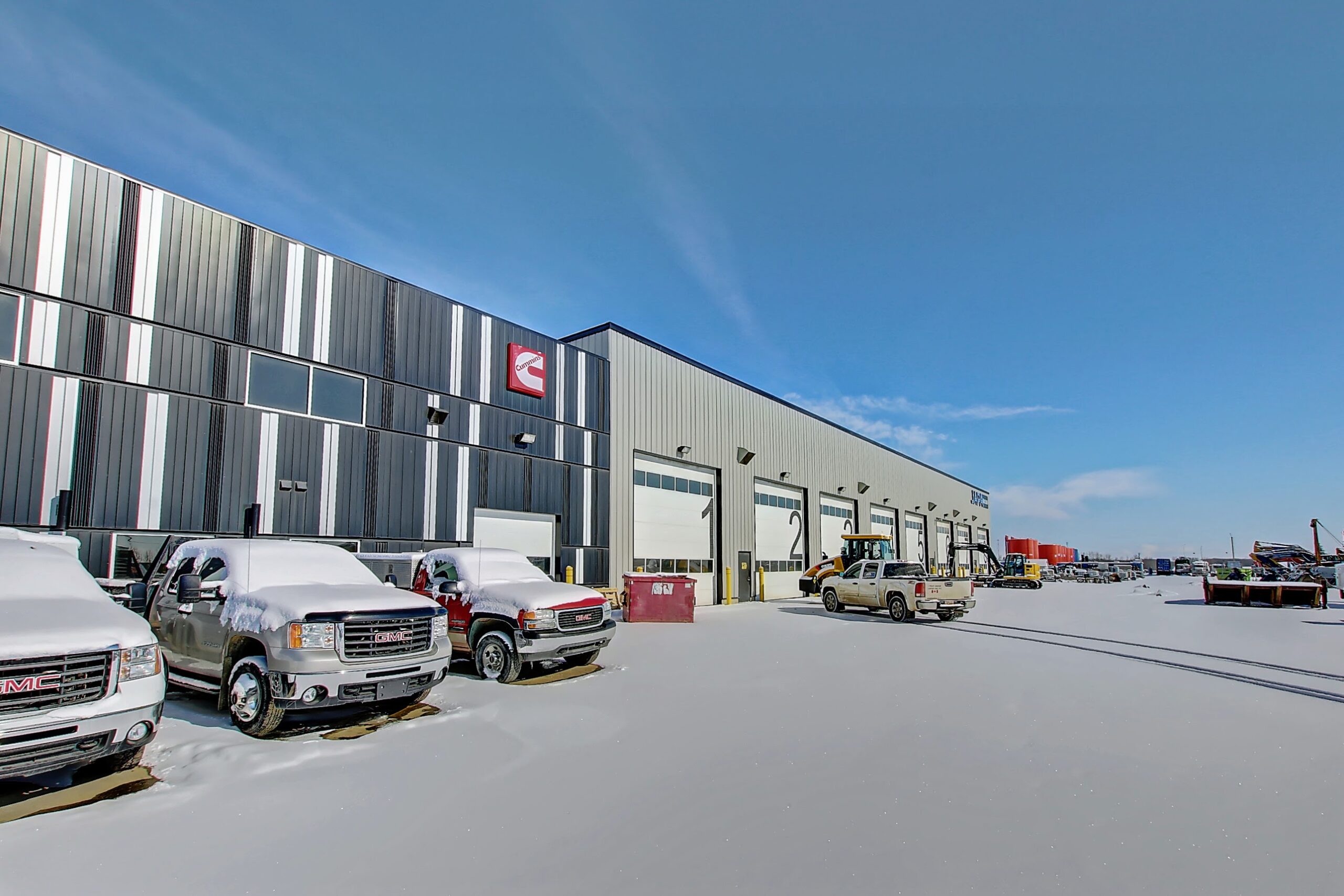 A snow-covered parking lot and the exterior of two buildings. The one on the left is the NCSG black and white building while the one on the right is the beige warehouse bays of JAPA Equipment Rentals.