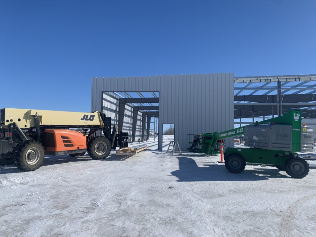 The exterior of an in-construction steel structure. Construction vehicles are outside the building.