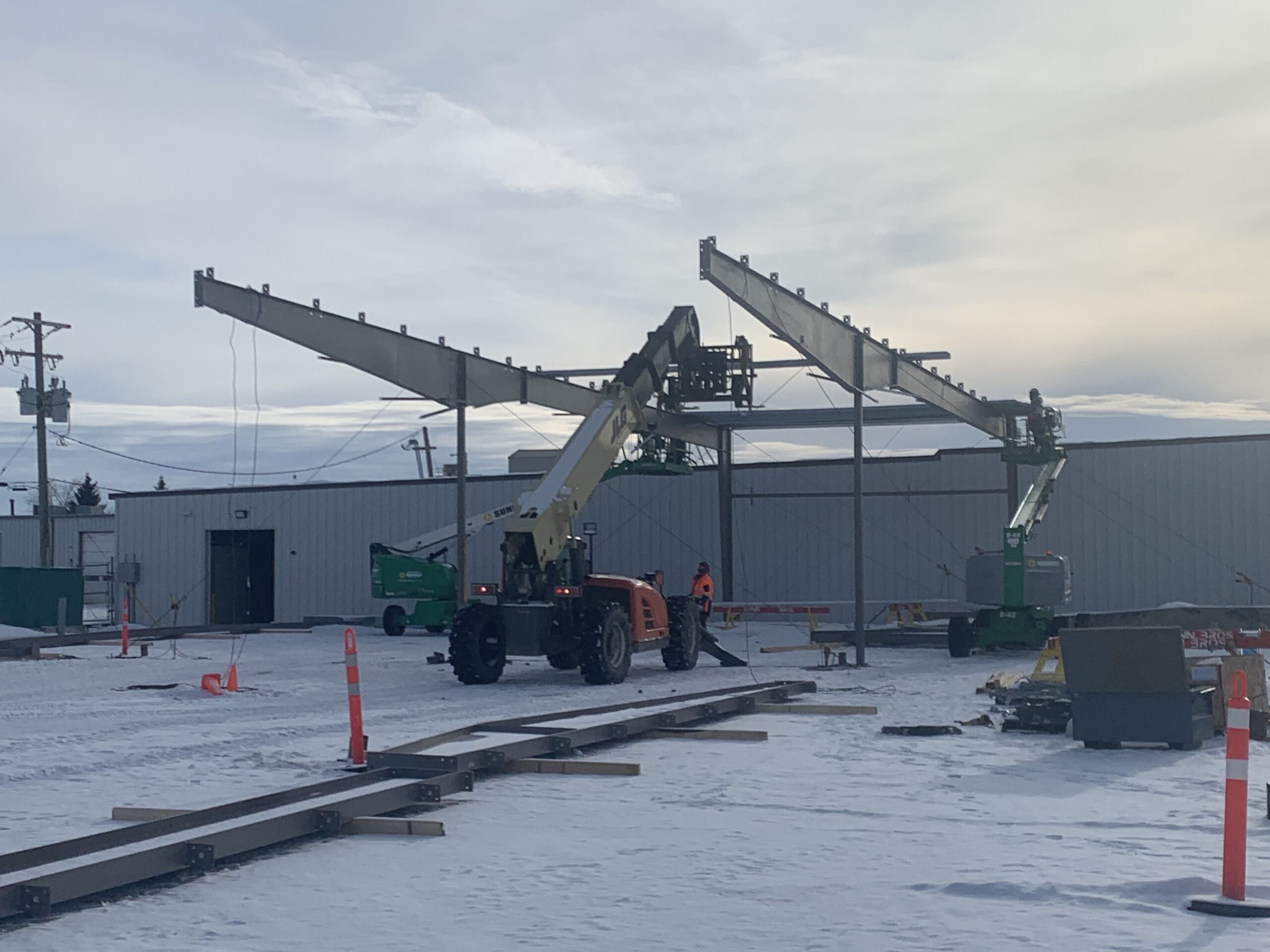 An orange telehandler lifts equipment onto a white fabricated steel structure.