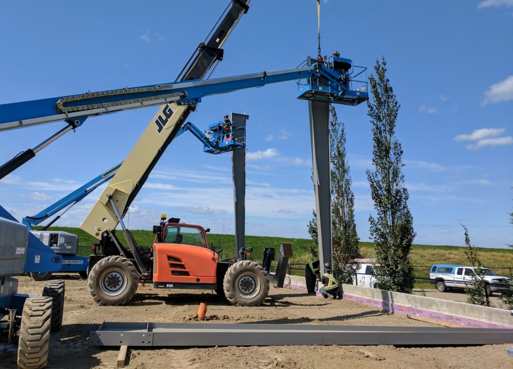 Workers operating two blue telehandlers working on the construction of a new commercial building.